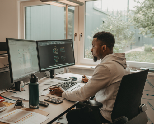 Mitarbeiter sitzt im Büro an einem Schreibtisch und arbeitet an zwei Monitoren mit CAD-Software